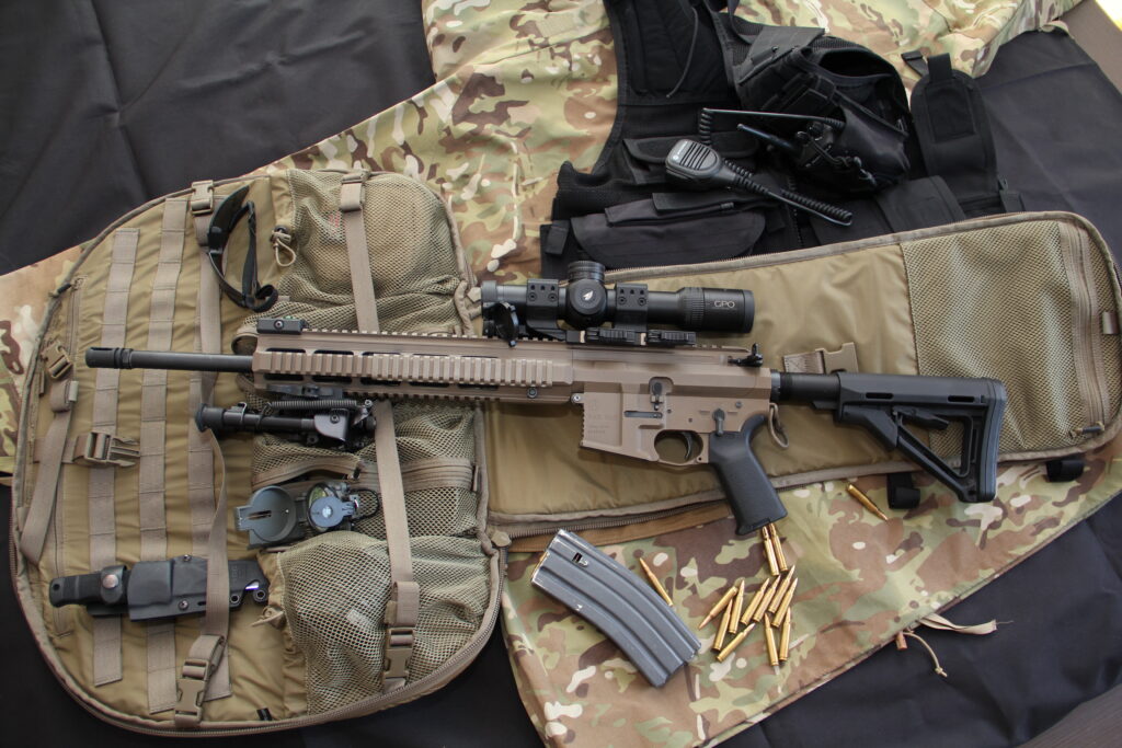 An AR with a GPO USA rifle scope on it sits on a tactical bag among other rifle accessories.