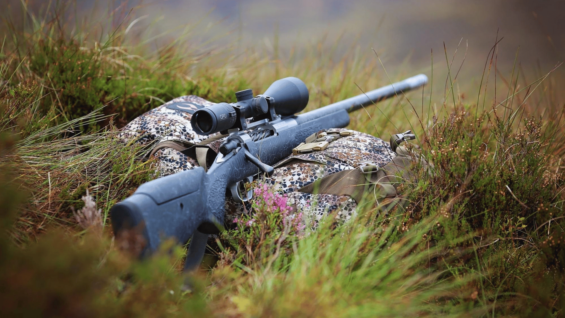 A hunting gun and scope resting on a camo bag in the feild 
