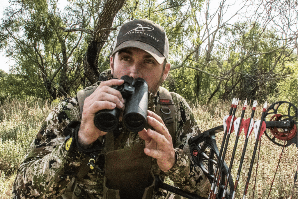 A man hunting with GPO binoculars in the forest getting ready to find a deer in camo