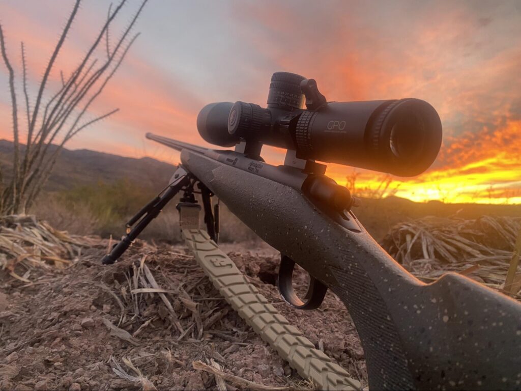 Gun propped up to be used in the feild during sunset with a rifle scope