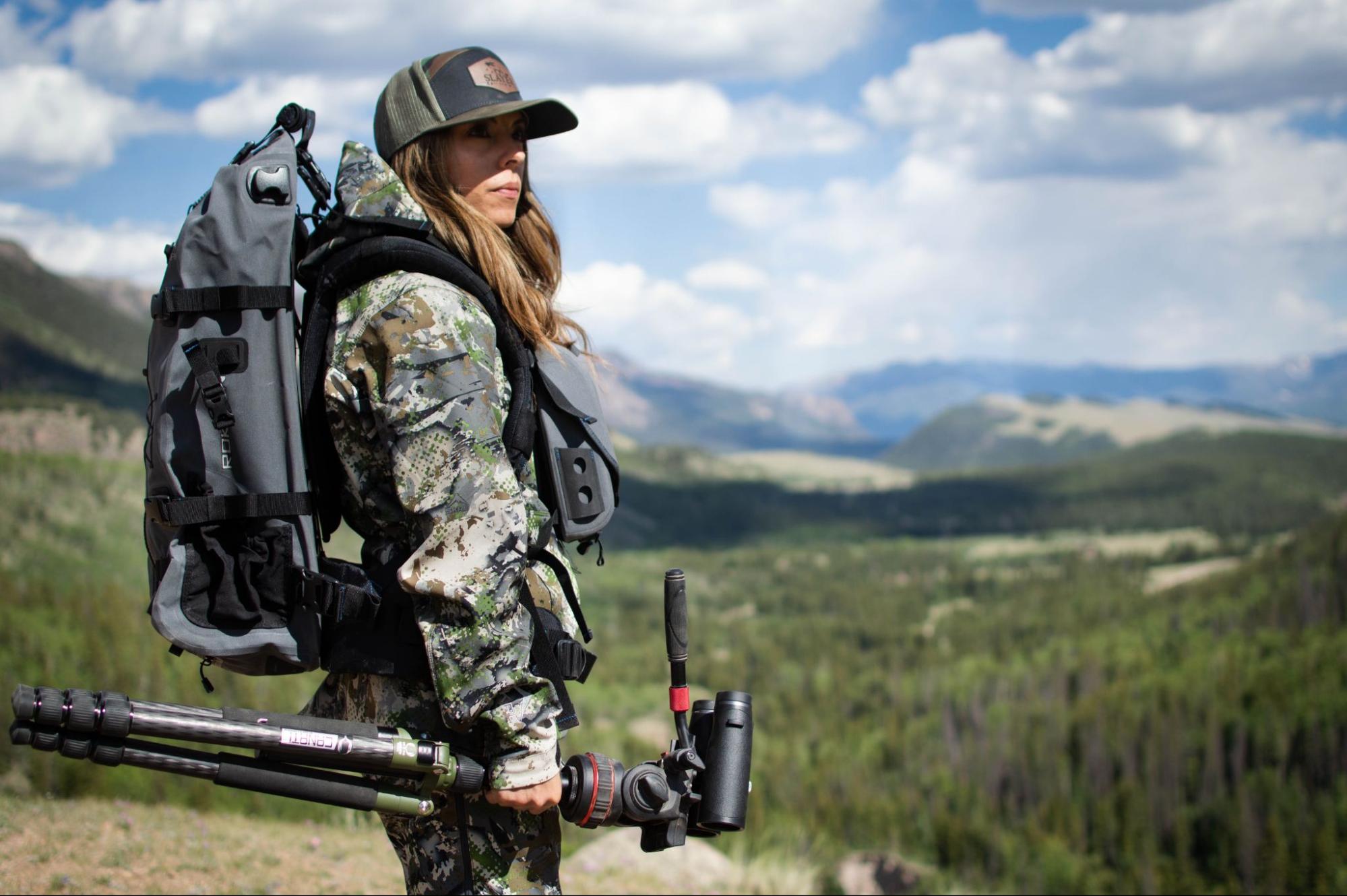 Women out hunting with hunting gear on like backpack, tent, hat, rifelscope, binoculars, and other hunting necessities.