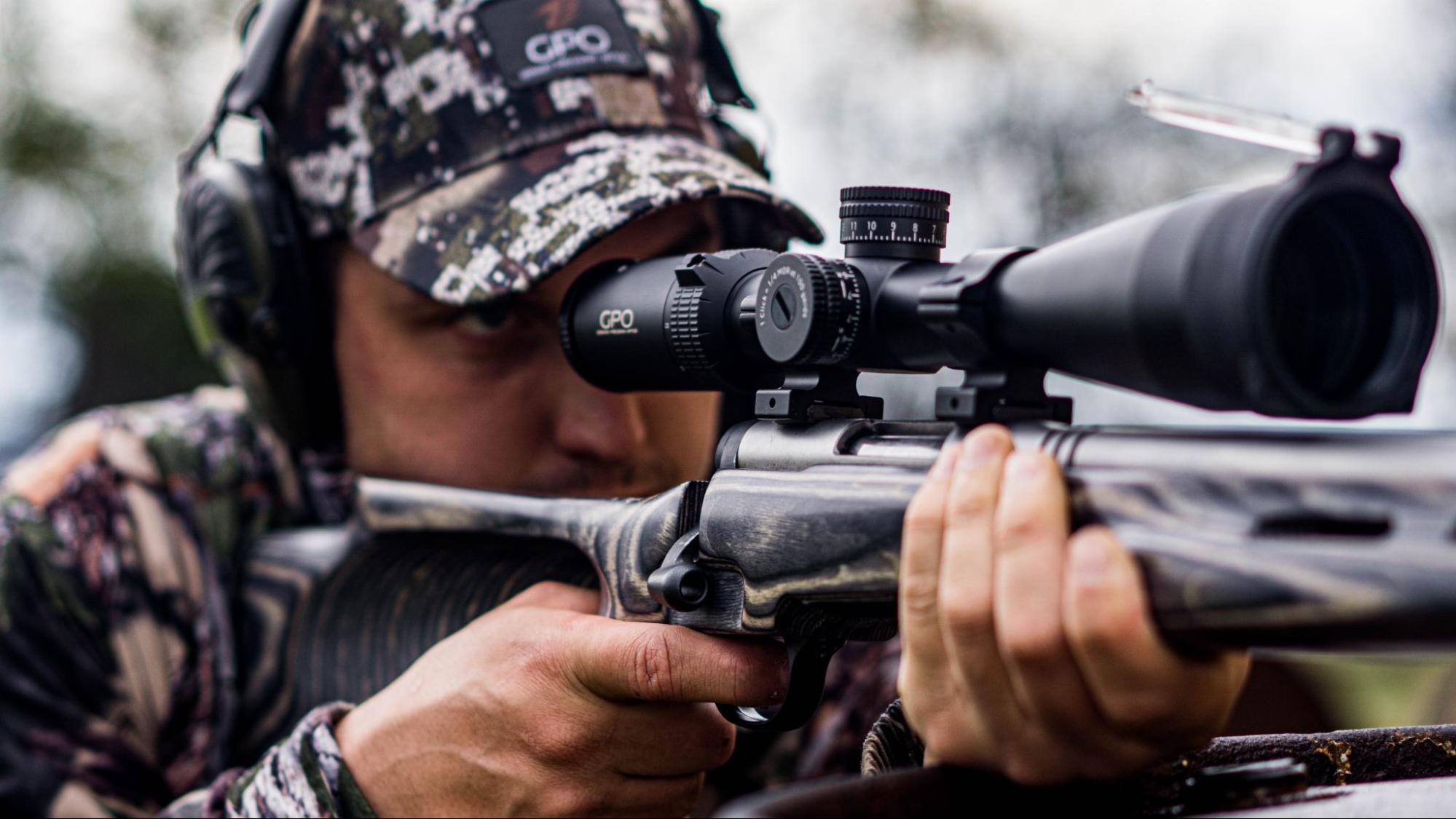 A close up of man in all camo hunting with a riflescope on rifle looking for his next hunt.